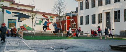 En lekplats utanför Dalaskolan med några gungor och barn som leker i bakgrunden.
