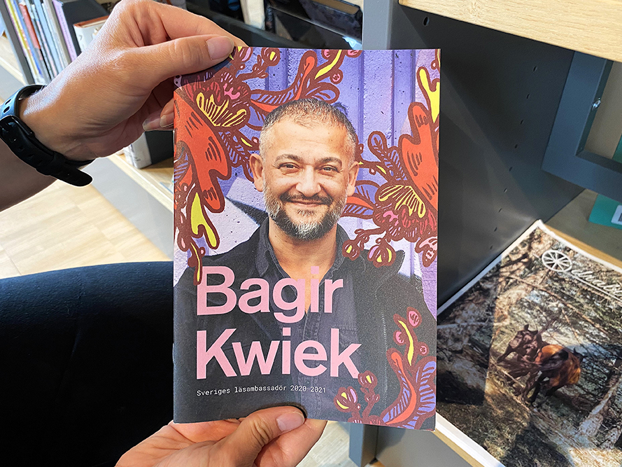 Foto av en folder med en person och illustrationer på omslaget, med texten "Bagir Kwiek".