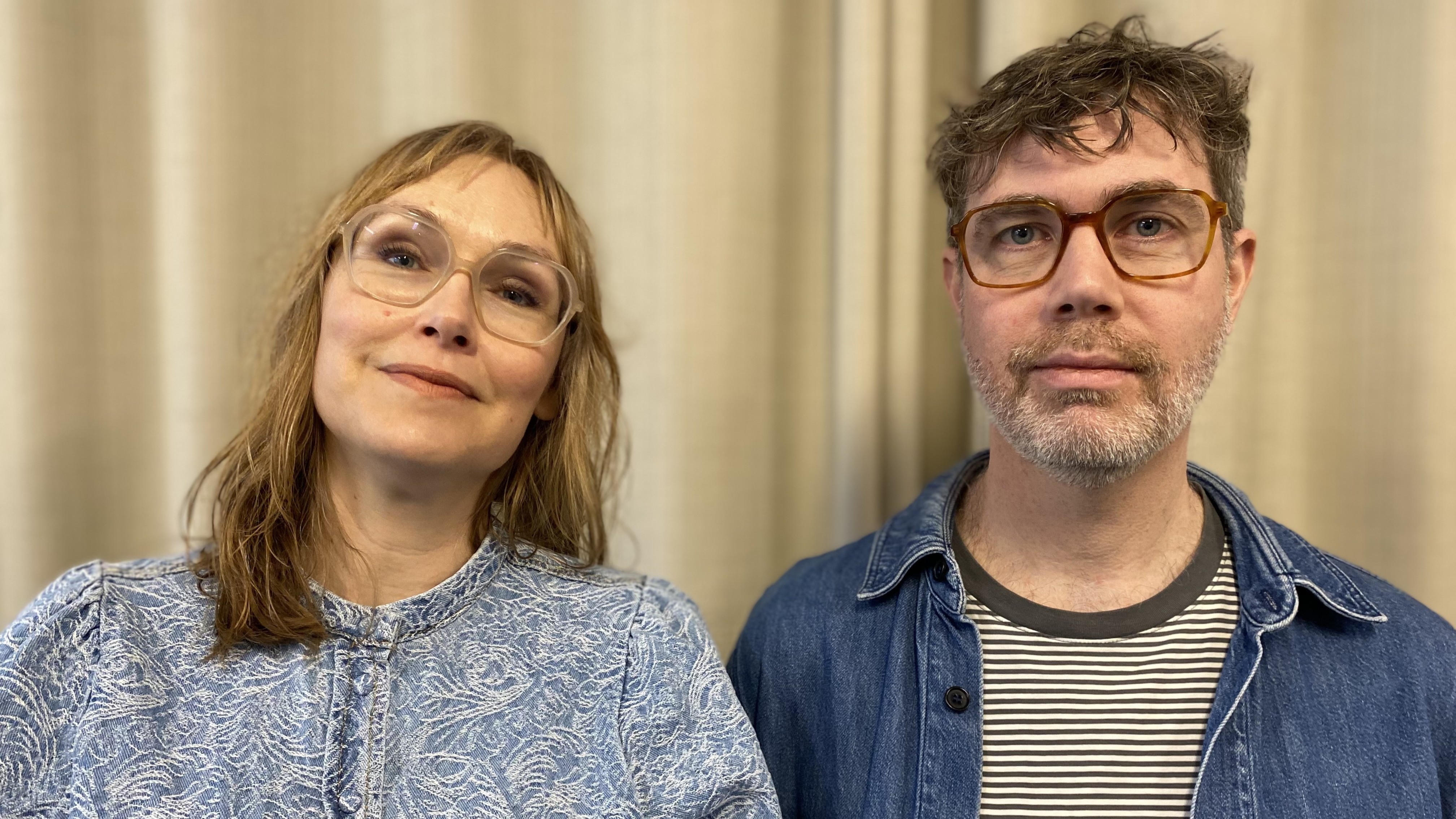Porträttbild av två personer, en med blont axellångt hår och glasögon, en med mörkt kort hår, skägg och glasögon