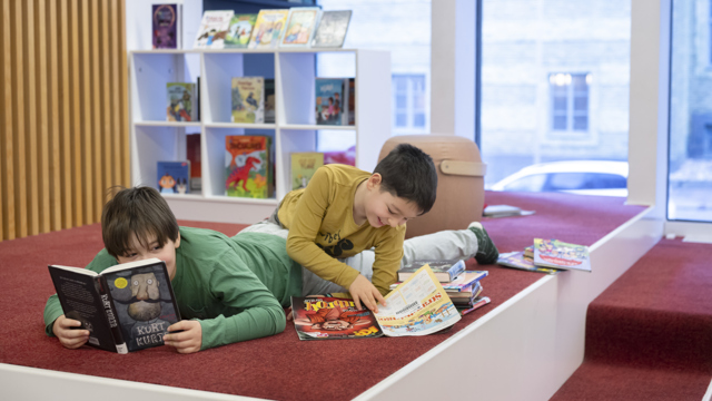 Två barn ligger och läser på ett bibliotek