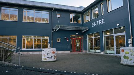 En skolbyggnad i grönblå färg med en entré