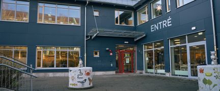 En skolbyggnad i grönblå färg med en entré