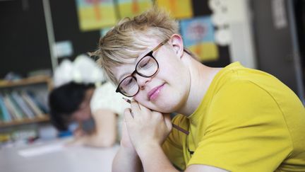 En elev sitter i ett klassrum och en annan elev syns bakom. 