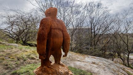 En gorilla i gjutjärn står på en liten bergsknalle framför ett bostadshus. Gorillan blickar upp mot skyn.
