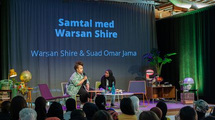 Två personer sitter på en scen och samtalar, i förgrunden publik