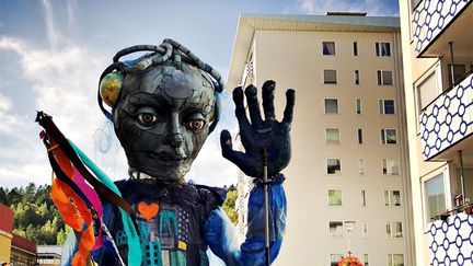 Stor figur i figurparad, till höger balkonger med blåvitt mönster