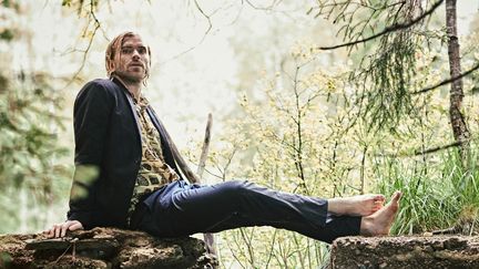 Person i mörkblå kläder som sitter på en sten i skogen