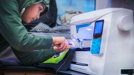  Ett foto av ett barn som böjer sig fram mot en symaskin och klipper av tråden med en sax.