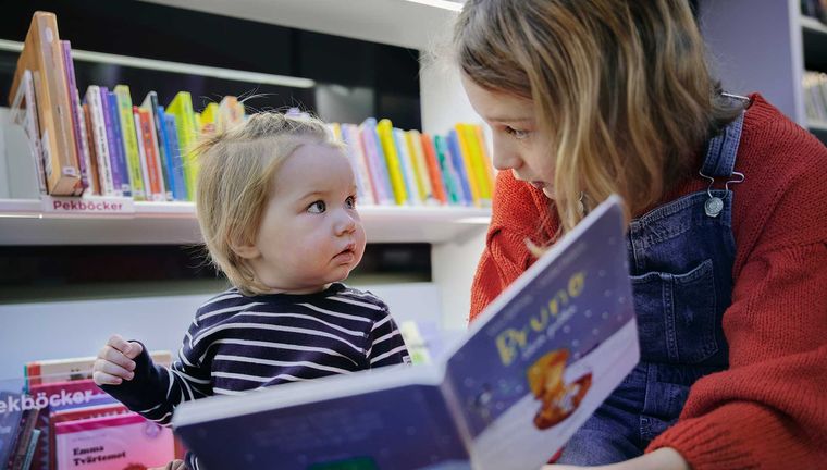 Större barn läser i bok med ett mindre barn.