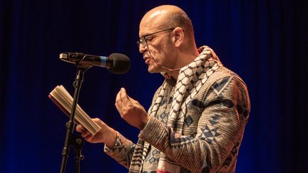 Foto av en person som läser ur en bok på scen