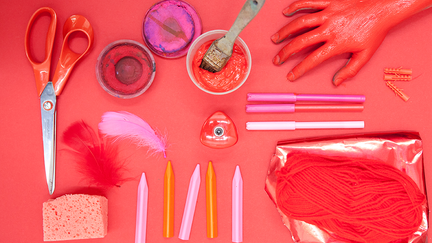 Foto av en sax, pennor och penslar på ett rött underlag