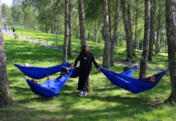 Ungdomar ligger i blå hängmattor bundna mellan träd i ett grönområde