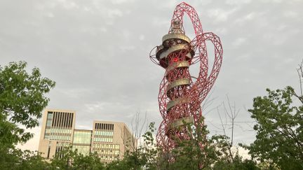 Väldig skulptur som vrider sig som en rymdfarkost med höga byggnader i bakgrunden och grönska i förgrunden
