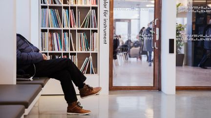 Bild på person som sitter ner inne på ett bibliotek.
