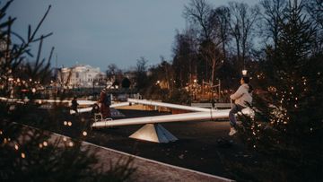 Personer som gungar på upplysta gungbrädor, med upplysta granar runt omkring.