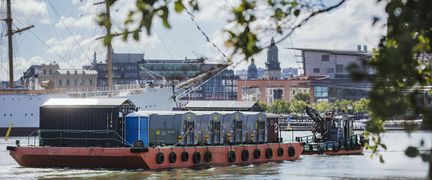 A barge floating on a river with the city in the background.