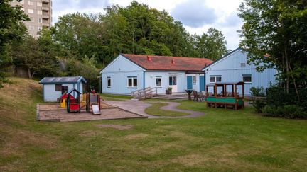 Familjecentralen Trädet har två vita trähus, en vit lekstuga och en liten lekplats.