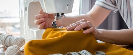 En person syr ett orange tyg med symaskin.