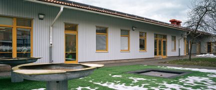 En lekplats syns i fokus med Hinnebäcksskolan i bakgrunden.