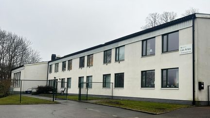 Ett långt vitt hus i två våningar. På gaveln en skylt med texten Las Artes. 