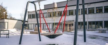 En gunga framför Bergsjöskolan med en skolbyggnad i bakgrunden.
