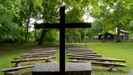 Träbänkar på rad framför ett altare i sten, utomhus.