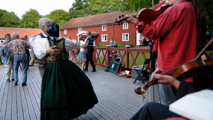 Människor som dansar i folkdräkter, och två som spelar fiol vid sidan.