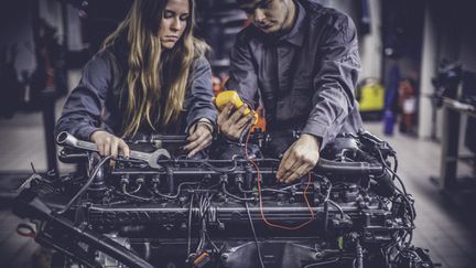 Två personer mekar med en motor.
