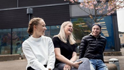 Tre glada elever under ett blommande körsbärsträd och framför en skolbyggnad.