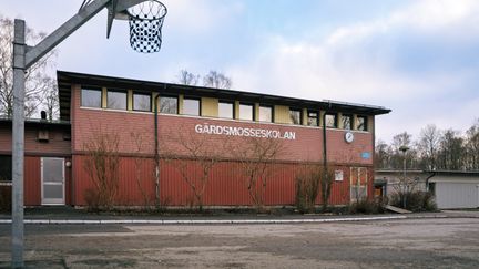 En basketkorg framför en röd skolbyggnad med texten Gärdsmosseskolan på fasaden.