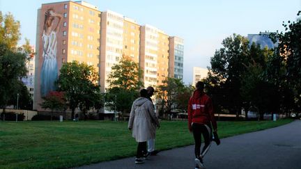 Ett höghus i frlölunda med tre personer som promenerar
