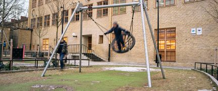 En lekplats framför Karl Johansskolan med ett barn som gungar i fokus.