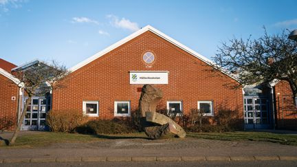 En skolbyggnad i rött tegel med skylten Hällsviksskolan på och en stor stenskulptur framför sig.