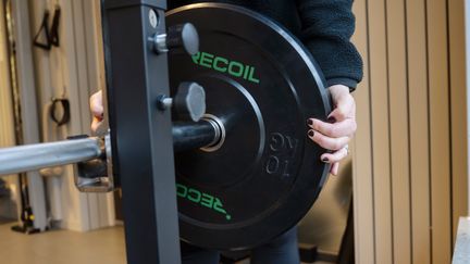 Händer sätter en viktskiva på en skivstång