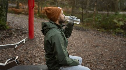 Person i mössa dricker vatten i en paus på utegymmet