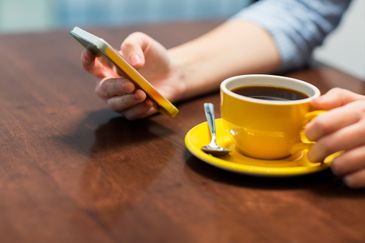 Närbild på en kvinna som håller sin smartphone i handen och dricker kaffe