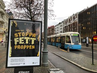 Bilden visar en spårvagn i Brunnsparken som passerar en reklamtavla med budskapet Hjälp oss stoppa fettproppen 