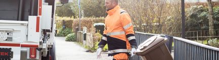 En renhållningsarbetare drar ett matavfallskärl till sopbilen.