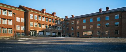 En tom skolgård framför en röd skolbyggnad i tegel.