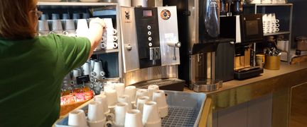 En person ställer in nya koppar på en hylla bredvid kaffemaskinen.