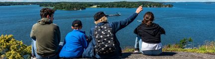 Fyra barn sitter på ett berg vid havet och pratar med varandra.