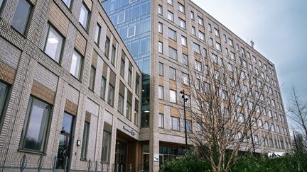 Överblick av Sandarnaskolans byggnader med huvudentrén och några träd i bakgrunden.