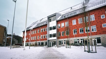 En röd skolbyggnad med en entré och en gåväg som leder fram till den