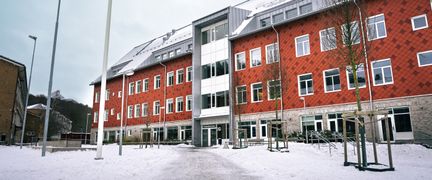 En röd skolbyggnad med en entré och en gåväg som leder fram till den