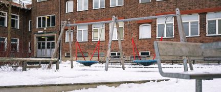 En gungställning framför en skolbyggnad i rött tegel.