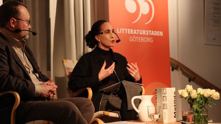 Två människor samtalar på en scen. Litteraturstaden Göteborgs symbol syns i bakgrunden. 
