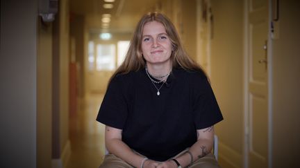 En person sitter med händerna i knät och tittar rakt emot betraktaren. 