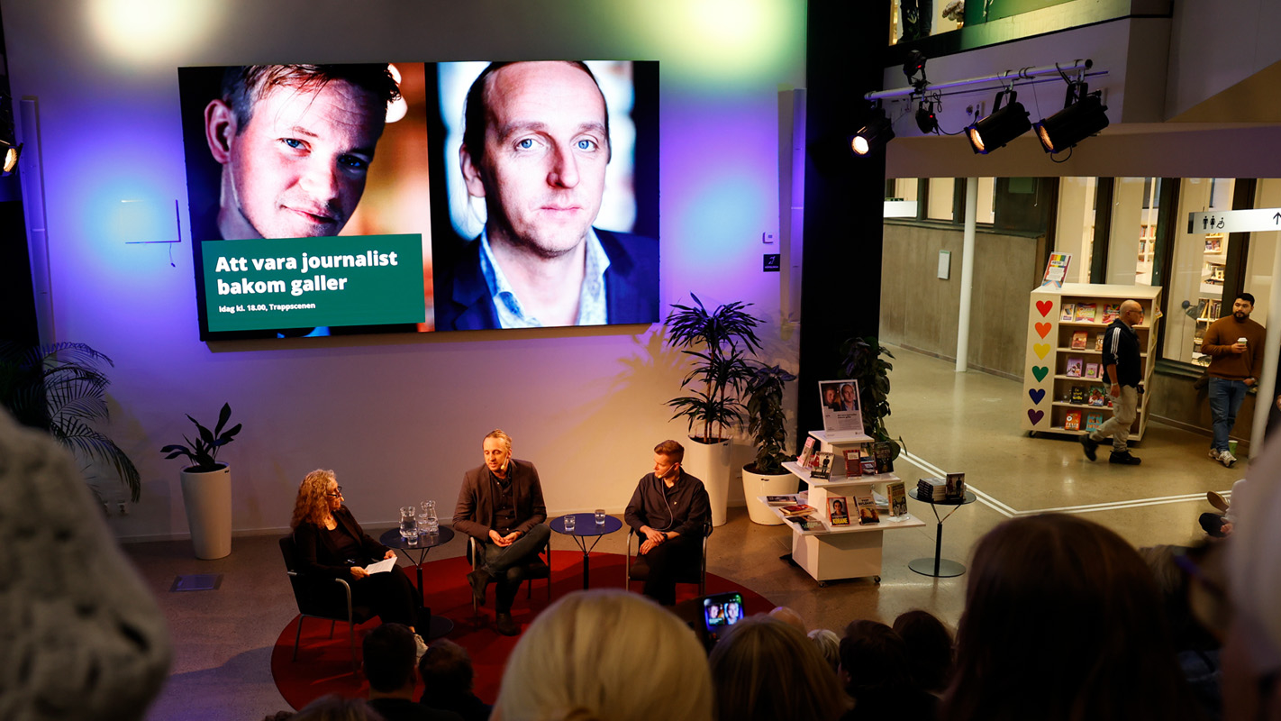 Three people on a stage in front of the title of the talk "To be a journalist behind bars".