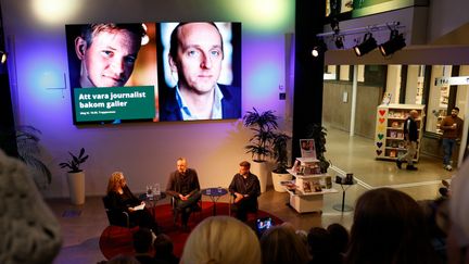Three people on a stage in front of the title of the talk "To be a journalist behind bars".