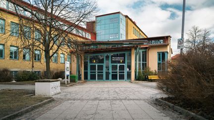 En entré till en skolbyggnad med texten Huvudentré Bjurslättsskolan på glasdörren och en gångväg som leder till den.